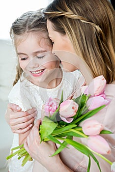 Happy mother with tulips hugging smiling daughter, mother`s day concept