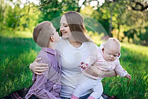 Happy mother with two children. Brother and sister with mummy in the Park. Mom hugging her son and holds baby