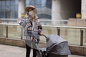 Happy Mother walking With Stroller In Park and using mobile phone. Joy of motherhood. Stylish young caucasian woman