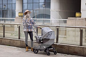 Happy Mother walking With Stroller In Park and using mobile phone. Joy of motherhood. Stylish young caucasian woman