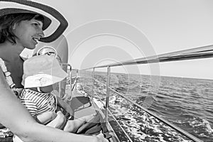 Happy mother wearing hat sitting with her baby on boat deck during cruise