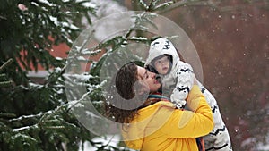 Happy mother on a winter walk in the park with the baby. It is snowing, the woman raises the child up laughing and