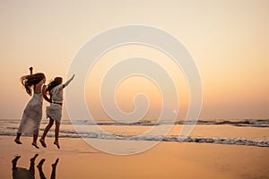 Happy mother and young daughter on the beach at sunset having fun at the seaside. playing jumping and rejoicing woman