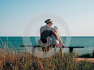 Happy motherand daughter sitting on bench with marine landscape view. Mom and child having fun walking together