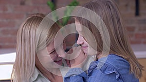 Happy motherhood, little smiling child girl tells beloved mum whispering secrets in ear at home