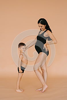 Happy motherhood. A pregnant woman in the studio on a beige background with her five-year-old son, measuring the size of their