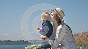 Happy motherhood, smiling cheerful mama in Hat with little child boy enjoying outdoors and watching on lake