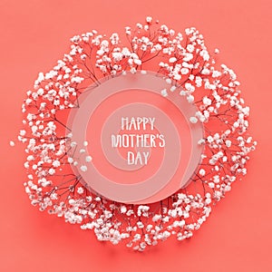 Happy Mothers Day Card. Flat lay greeting card with beautiful little white flowers on living coral pantone color paper background.