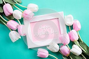 Happy mothers day concept. Top view of pink tulip flowers and white picture frame with happy mother`s day text on green pastel