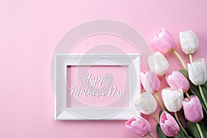 Happy mothers day concept. Top view of pink tulip flowers and white picture frame with happy mothers day text on pink pastel