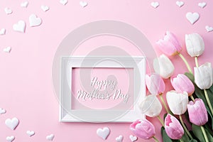 Happy mothers day concept. Top view of pink tulip flowers and white picture frame with happy mothers day text on pink pastel