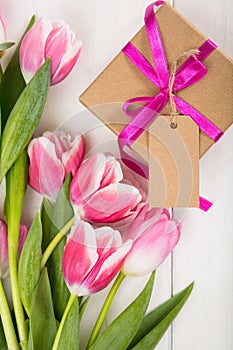 Happy Mothers Day concept. Top view of pink tulips bouquet and gift with blank card on white wooden background, copy space