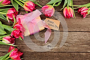 Happy Mothers Day gift and tag with corner border of pink flowers against a rustic wood background