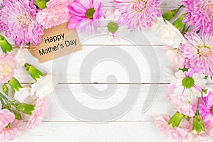 Happy Mothers Day gift tag with frame of flowers on a white wood background