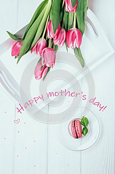 Happy mothers day greeting card. Pink spring tulips and raspberry macaron on a white background. Top view