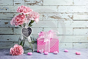 Happy mothers day message on heart wood and pink carnation flower in clear bottle and gift box