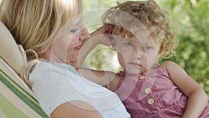 Happy mothers day smiling mom hugs and caresses her blue eyed little girl daughter child with curly blonde hair, together lying on