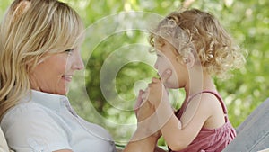 Happy mothers day, smiling mom playing with her blue eyed little girl daughter child with curly blonde hair, together lying on