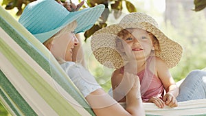 Happy mothers day, smiling mom playing with her blue eyed little girl daughter child, plays with her by putting on a big straw hat