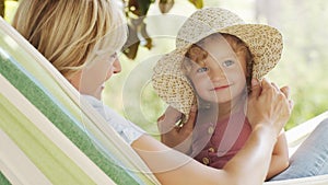 Happy mothers day, smiling mom playing with her blue eyed little girl daughter child, plays with her by putting on a big straw hat