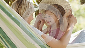 Happy mothers day, smiling mom playing with her blue eyed little girl daughter child, plays with her by putting on a big straw hat