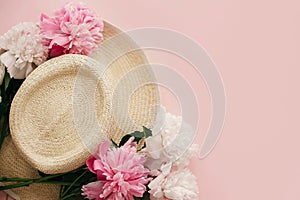 Happy mothers day. Straw hat with white and pink peonies on pastel pink paper, flat lay. Hello spring image with copy space.