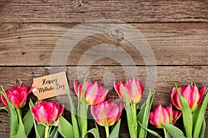 Happy Mothers Day tag with bottom border of pink flowers against a rustic wood background