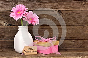 Happy Mothers Day tag with gift and pink flowers against rustic wood