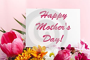 Happy Mothers Day text on gift card in flower bouquet on pink background. Greeting card for Mom. Flower delivery, Congratulations
