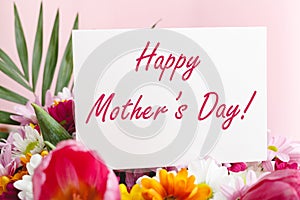 Happy Mothers Day text on gift card in flower bouquet on pink background. Greeting card for Mom. Flower delivery, Congratulations