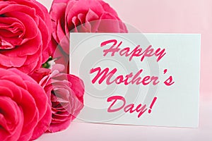 Happy Mothers Day text on gift card in flower bouquet of pink roses on pink background. Greeting card for Mom. Flower delivery,