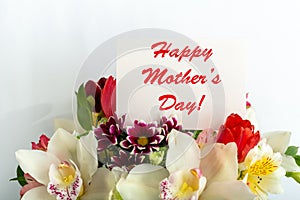 Happy Mothers Day text on gift card in flower bouquet on white background. Greeting card for Mom. Flower delivery, Congratulations