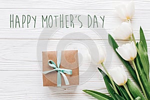 happy mothers day text sign on stylish craft present box and tulips on white wooden rustic background. flat lay with flowers and