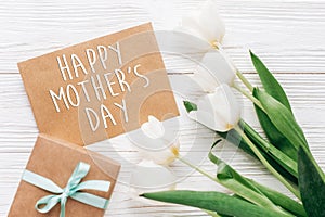 happy mothers day text sign on stylish craft present with greeting card and tulips on white wooden rustic background. flat lay wi