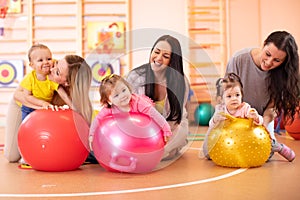 Happy mothers and their babies on fitness ball in nursery. Gimnastics for kids on fitball.