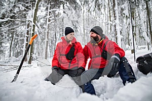 Happy mountain rescue service on operation outdoors in winter in forest, digging snow with shovels.