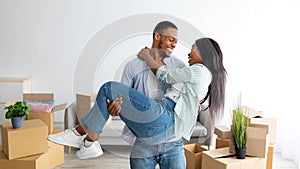 Happy moving day. Loving african american couple celebrating relocation, husband lifting his wife up on hands, panorama