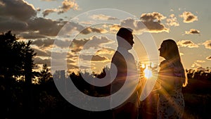 Happy multi-ethnic couple drinking wine at sunset. They stand near the vineyard. Honeymoon and travel concept