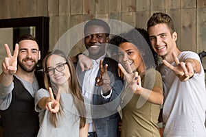 Happy multi-ethnic young people showing peace sign looking at ca