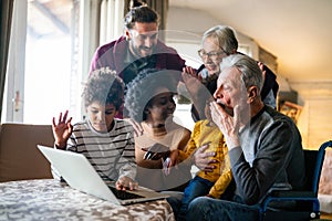 Happy multi-generation family gathering around notebbok and having fun during a video call