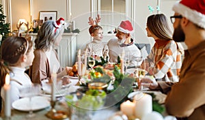 Happy multi generation family in Santa hats at dinner table, saying xmas toasts and clinking glasses