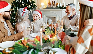 Happy multi generation family in Santa hats at dinner table, saying xmas toasts and clinking glasses