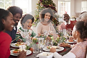 Happy multi generation mixed race family sitting at their Christmas dinner table eating and talking, selective focus