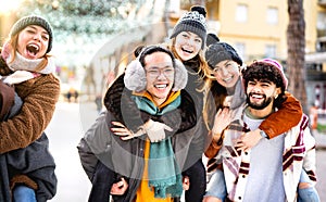 Happy multicultural friends walking at winter travel location on piggyback move - Everyday life style concept