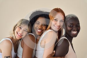 Happy multicultural girls in underwear hugging on beige background, portrait.