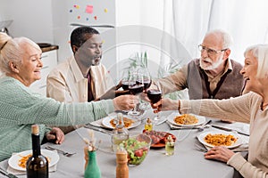 happy multicultural pensioners clinking glasses of