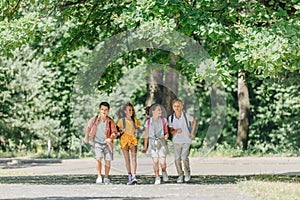 Happy multicultural schoolkids with backpacks running in sunny park