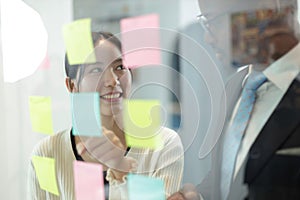 Happy multiethnic business team meeting pointing at post it notes on glass board. business team meeting brainstorm share idea at