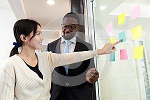 Happy multiethnic business team meeting pointing at post it notes on glass board. business team meeting brainstorm share idea at