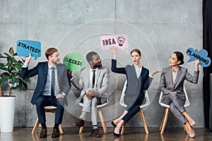 Happy multiethnic businesspeople holding speech bubbles with idea, success, planning and strategy lettering while sitting in